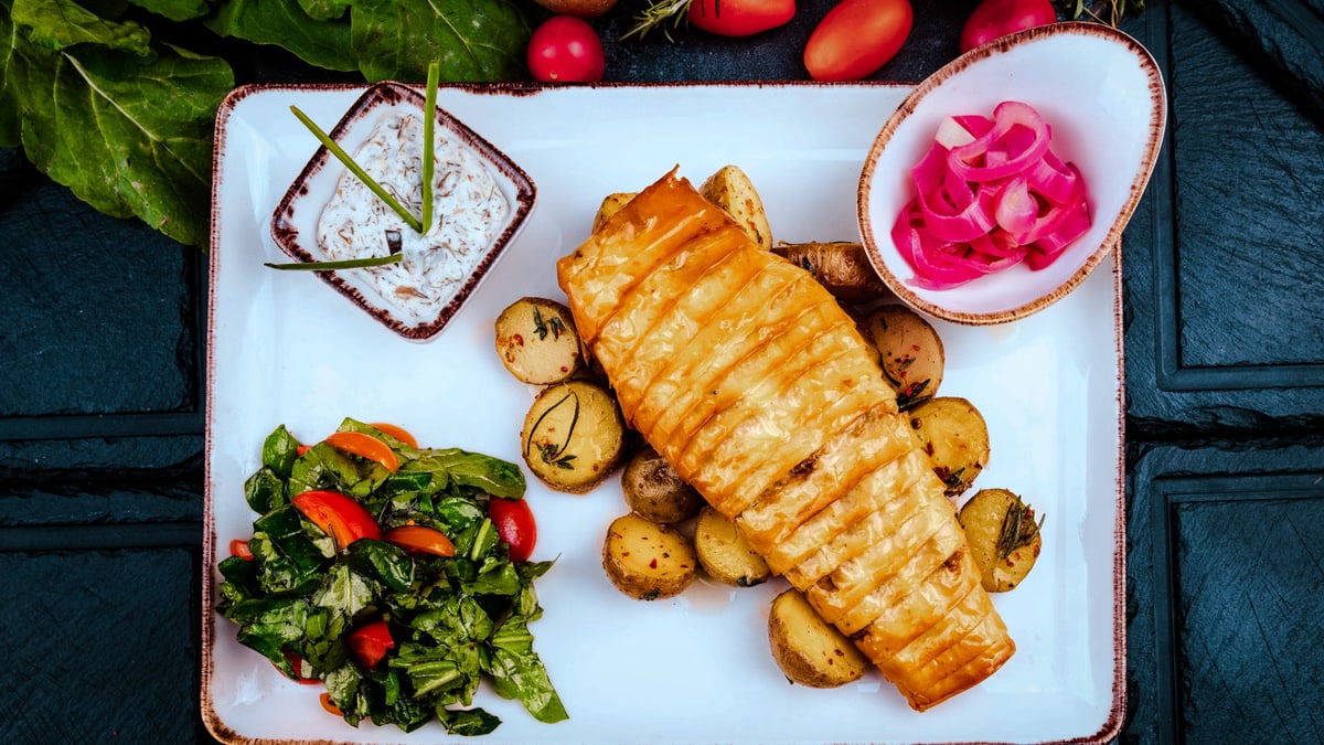 Delicious roasted fish with potatoes and fresh vegetables served on a white platter.